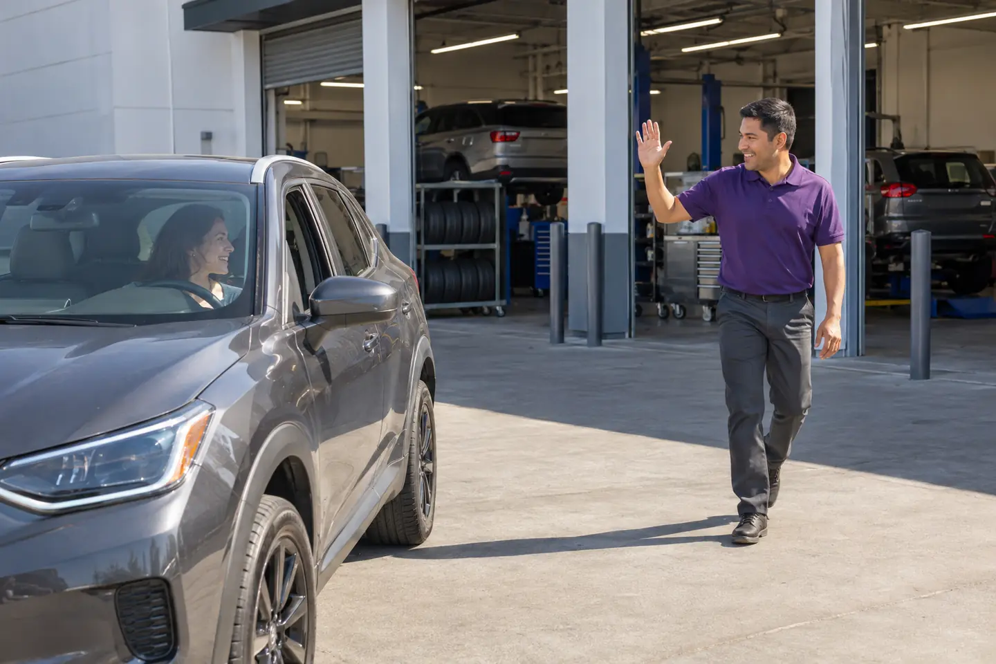 A store associate waves as a customer parks in front of the service bays