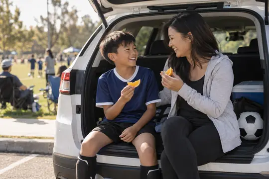 A mother and son share orange slices on their car’s open hatch after soccer