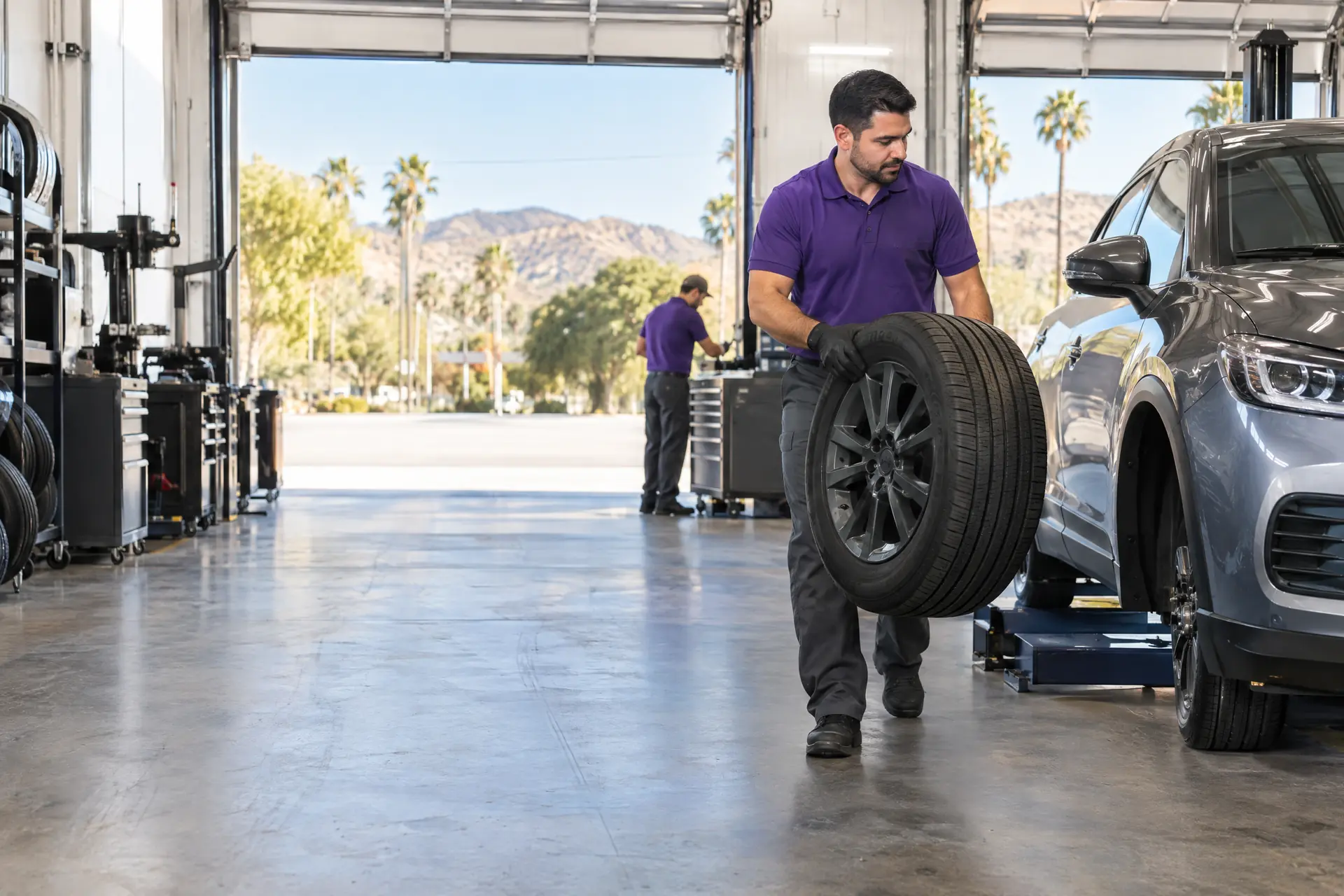 A technician carrying a wheel through an open service bay on a sunny morning